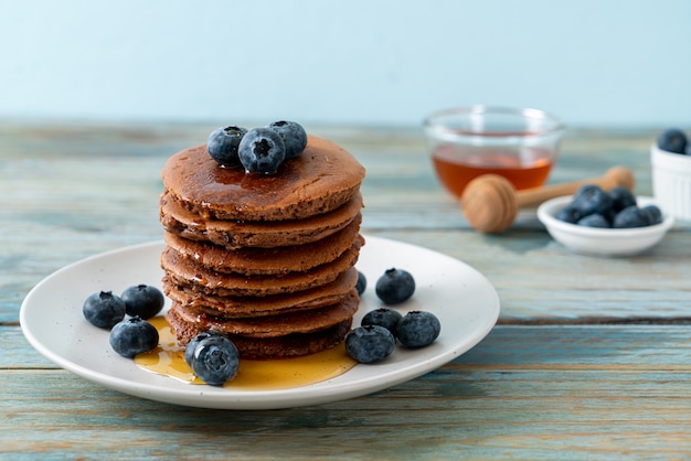 De stapel van de chocoladepannekoek met bosbessen en honing op plaat