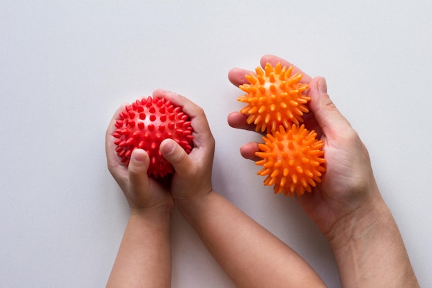 De stekelige rode bal van de massagenaald in kinderhanden en twee sinaasappelenballen in vrouwenhand op de witte achtergrond
