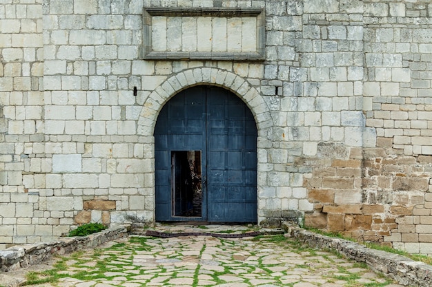 De stenen muur met een oude ijzeren poort op de donkere kleur. De hoofdingang van het fort Khotyn.