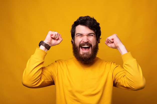 De sterke gebaarde mens maakt het winnaargebaar met beide handen op gele achtergrond.