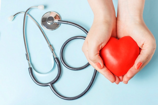 De stethoscoop en het rode hart in vrouwelijke handen sluiten omhoog op blauwe achtergrond