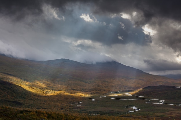 De stralen van de zon breken door de donkergrijze wolken. Indrukwekkend uitzicht op de bergen van het nationale park Sarek in Zweeds Lapland. selectieve aandacht