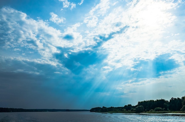 De stralen van God in het rivierlandschap. De zonnestralen schijnen door de wolken over het wateroppervlak en de kust. Ruimte kopiëren