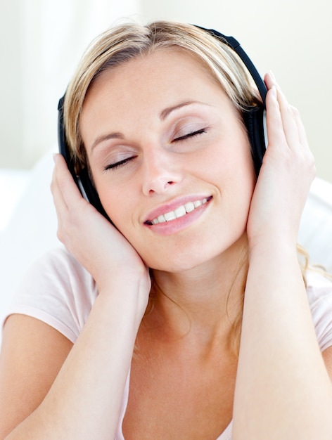 De stralende jonge vrouw luistert aan muziek die hoofdtelefoons draagt