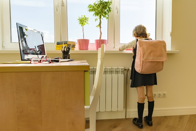 De studente van het meisje met rugzak in schooluniform kijkt uit het venster