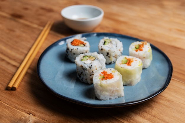 de sushi rollen groente op blauwe plaat met eetstokjes en sojasaus in witte kom op houten lijst.