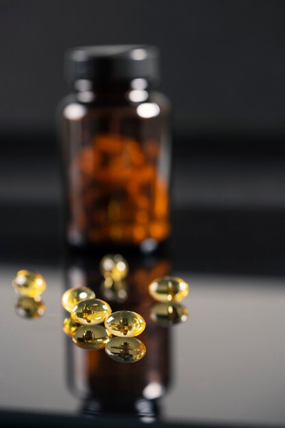 De tabletten liggen op een gespiegelde zwarte achtergrond, reflecteren erin. Donkere fles met medicijnen onscherp.