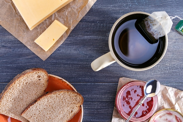 De tafel klaarmaken voor ontbijt. Kopje thee en brood met kaas, pot jam.