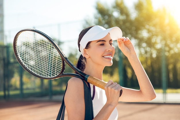 De taille van een mooie jonge tennisspeler in een witte pet.