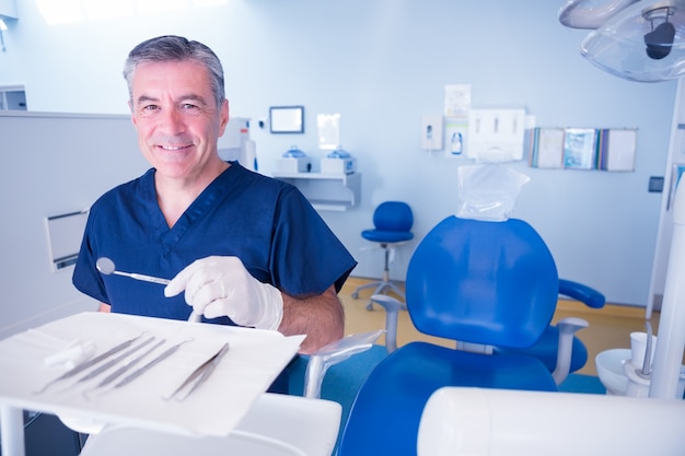 De tandarts in blauw schrobt het glimlachen bij de hulpmiddelen van de cameraholding
