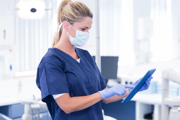 De tandarts in masker en blauw schrobt gebruikend haar tablet