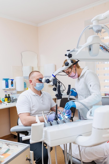 De tandarts is in zijn tandartspraktijk Een tandarts in een wit uniform behandelt de tanden van een patiënt met een tandheelkundige microscoop Tandartspraktijk