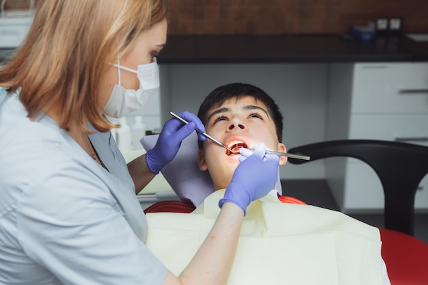 De tandarts onderzoekt de tanden van een jongen van 13 jaar oud in de kliniek pediatrische tandheelkunde