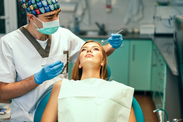 De tandarts onderzoekt vrouwelijke patiënt met steunen in denikantoor.