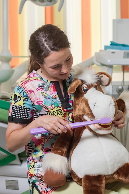 Foto de tandarts van een jong meisje dokter kinderen laat zien hoe tanden op speelgoed te poetsen