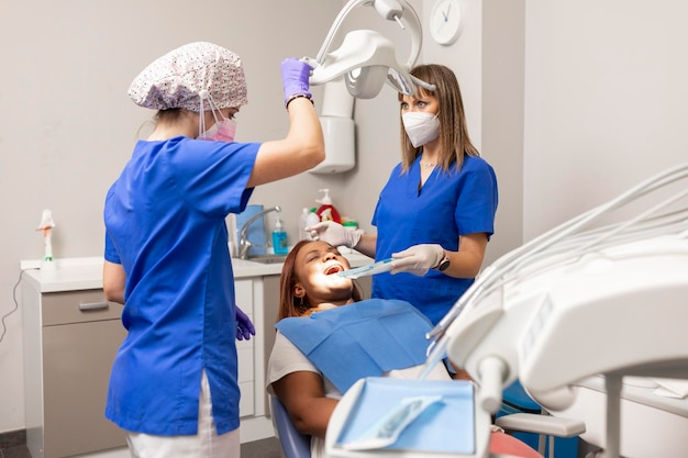 De tandartsvrouw past het tandheelkundige operatielampje aan terwijl de cliënt in de tandartsstoel ligt