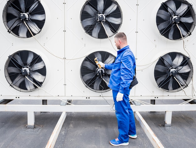 De technicus gebruikt een infraroodthermometer met thermische beeldvorming om de warmtewisselaar van de condensoreenheid te controleren