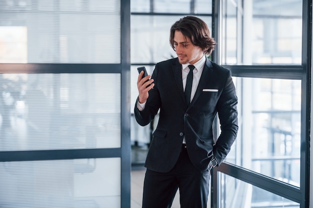 De telefoon gebruiken. Portret van knappe jonge zakenman in zwart pak en stropdas.