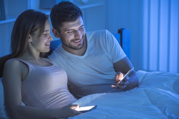 De telefoon van het glimlachpaar in de slaapkamer. nachttijd