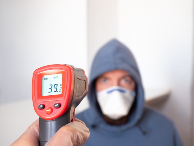 De temperatuur van een man meten met een infraroodmeter. Hoge koorts, symptoom, ziekte.