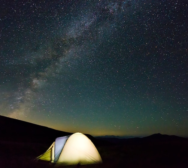 De tent van toeristenwandelaars in bergen bij nacht met melkwegsterren in de hemel