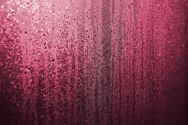 De textuur van beslagen glas met veel druppels en druppels condens tegen het zonlicht bij zonsopgang Achtergrondafbeelding Afbeelding afgezwakt in Viva Magenta kleur van het jaar