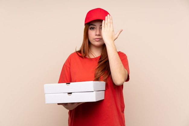 De tiener die van de pizzakoerier een pizza over geïsoleerde muur houdt die een oog met de hand behandelt