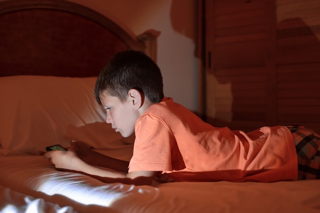 De tiener speelt een spelletje op een mobiele telefoon terwijl hij ontspant in een hotelkamer