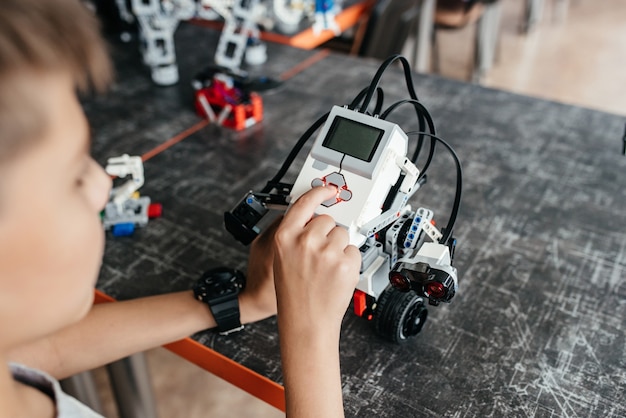 De tiener speelt met de robot aan de tafel.