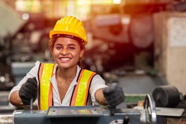 De tienerarbeider van het meisje met veiligheidshelm gelukkige het glimlachen werkende arbeid in de industiefabriek met staalmachine.