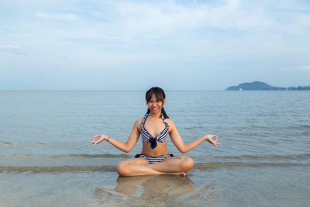 De tienermeisjes die van Azië de meditatie van de bikinizitting dragen bij het strand.