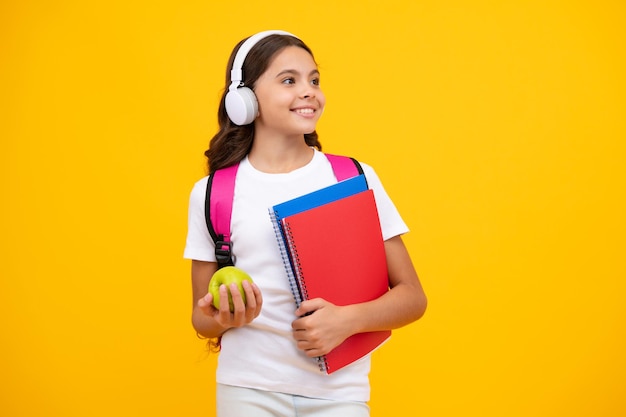 De tienerstudent van het schoolmeisje in hoofdtelefoons houdt boeken op gele geïsoleerde studioachtergrond School