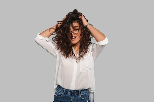 De tijd stopt als je naar haar kijkt. Aantrekkelijke jonge vrouw die met haar haar speelt en glimlacht terwijl ze tegen een grijze achtergrond staat