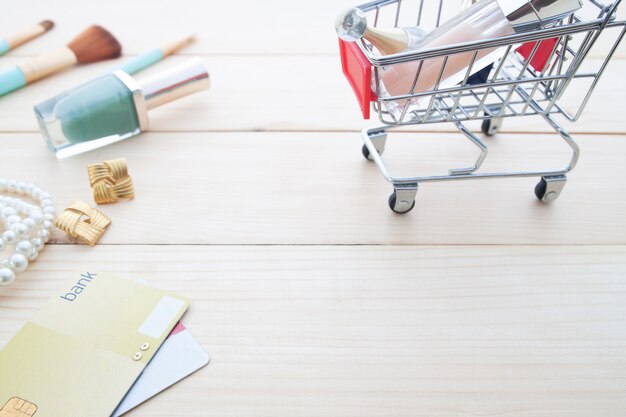 De toebehoren en de schoonheidsmiddelen van de vrouw in boodschappenwagentje met creditcard op houten lijst,