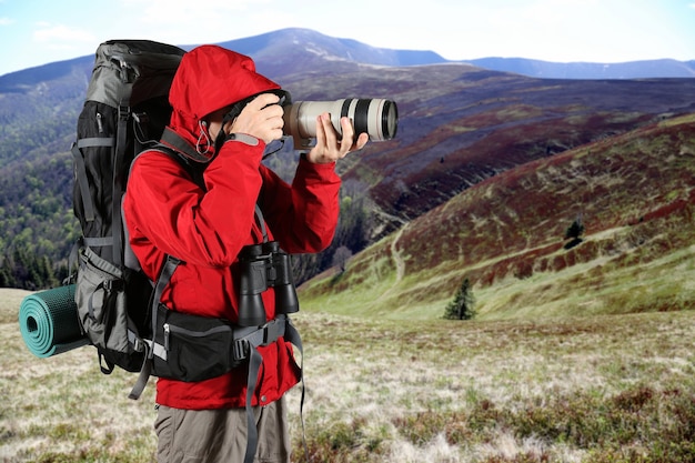 De toerist in een rood jasje met een grijze rugzak die foto's maakt