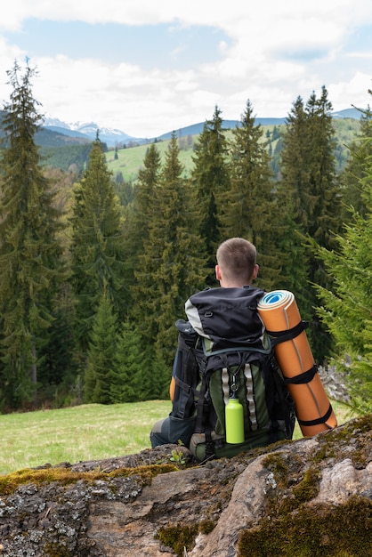 De toerist met een rugzak achter hem zit rustend op een opening van een sessie een open plek voor het bos