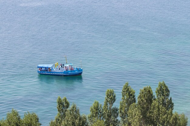 De toeristenboot met toeristen aan zee vlakbij de kust met groene bomen