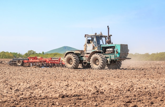 De tractor ploegt de grond met een cultivator die kluiten in de bedden verplettert en het veld klaarmaakt voor het zaaien in de lente.