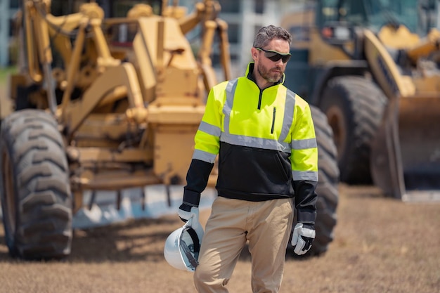 De tractor van de graafwerktuiglader en de man van de bouwerarbeider met helmarbeider bij bouw nieuw b