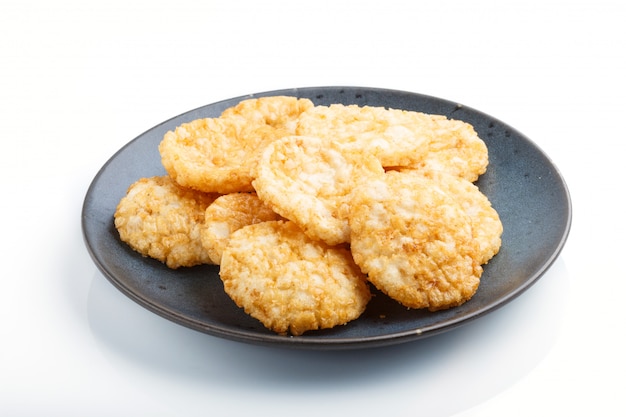 De traditionele japanse koekjes van rijstspaanders met honing en sojasaus op een blauwe ceramische plaat die op witte achtergrond wordt geïsoleerd