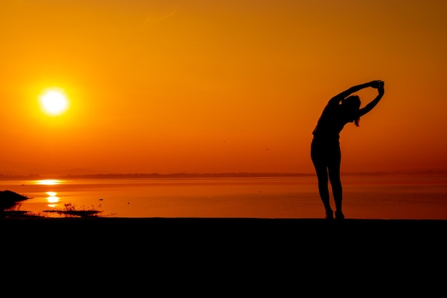 Foto de training van de silhouetvrouw alleen met zonsondergangachtergrond. gezonde en solo-oefenactiviteit. wellness levensstijl en openluchtrecreatie.