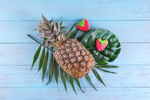 De tropische ananas met eigengemaakte verglaasde koekjes diende op palmbladen op blauwe houten achtergrond.