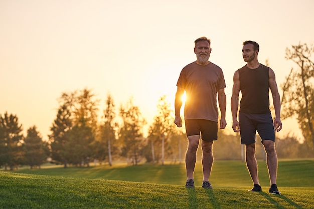 De twee sporters die zich op het gras op de zonsondergangachtergrond bevinden