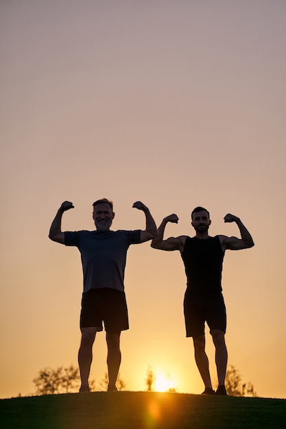 De twee sporters tonen spieren op de zonsondergangachtergrond