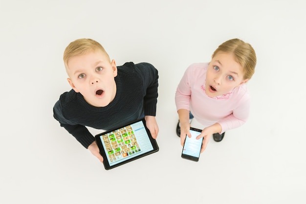 De twee verraste kinderen staan met apparaten. Uitzicht van boven