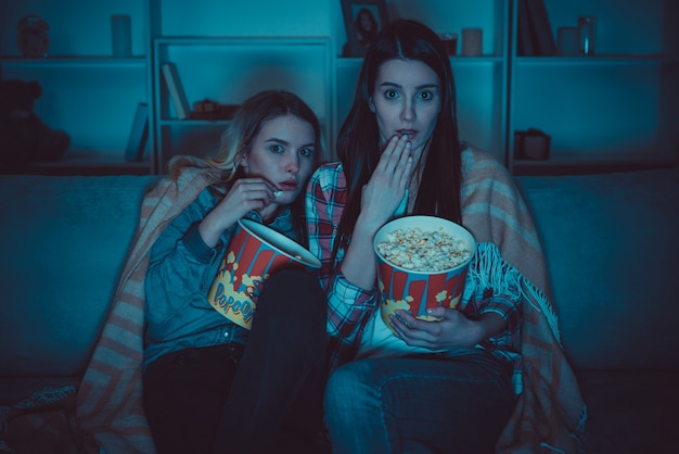 De twee vrouwen met een popcorn kijken een horrorfilm op de bank