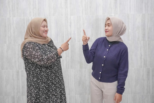 De uitdrukking van twee Aziatische Indonesische vrouwen met hijabs die blauwe en grijze kleren met wit dragen