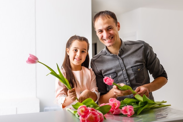 De vader houdt op zijn handen klein meisje op lichte achtergrond binnen. Portret van vader met bloemen en dochter. Het concept van gezinsvakantie. Vaderdag. bovenste helft. Detailopname.