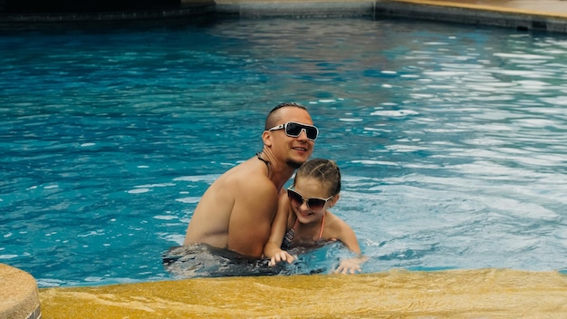 De vader met kleine dochter heeft plezier in het zwembad Papa speelt met het kind De familie geniet van de zomervakantie in een zwembad springend draaiend spatwater Slow motion