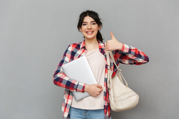 De verbazende emotionele jonge damestudent die laptop computer tonen maakt duimen omhoog gebaar.